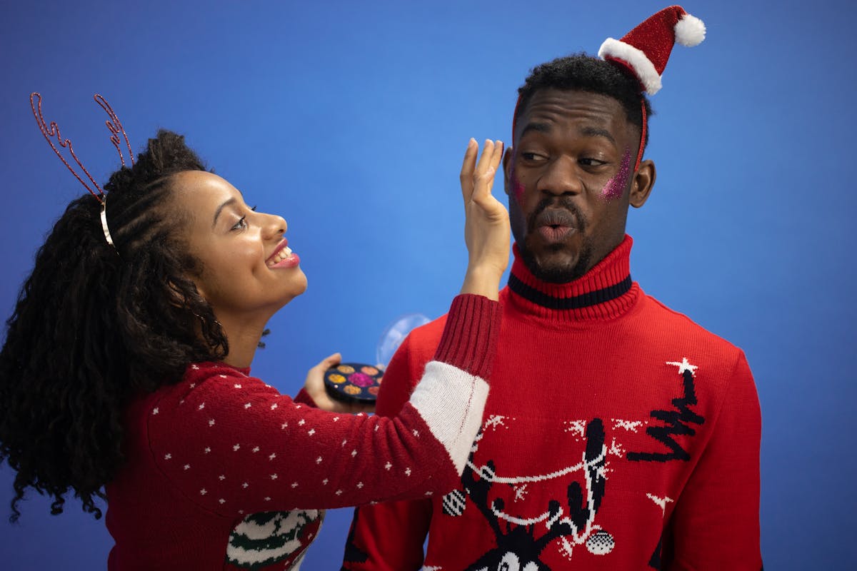 10 Odd Habits That Make Relationships Stronger 2 Joyful couple celebrating Christmas with festive makeup against a blue background.