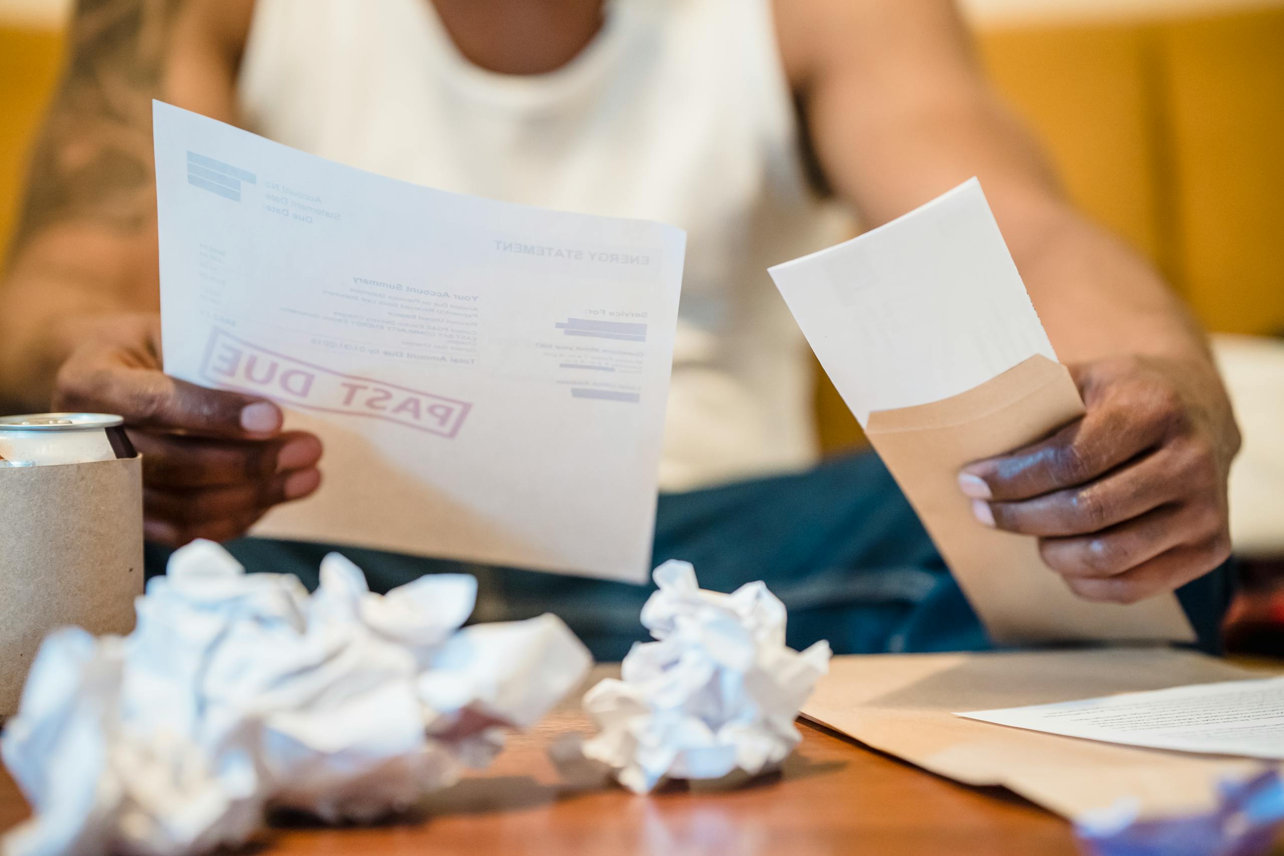 $25 Minimum Wage Bill Ignites America’s Cost-of-Living Fight as Workers Say One Job No Longer Pays Enough 1 Man sitting indoors reviewing past due bills with crumpled papers on a coffee table.