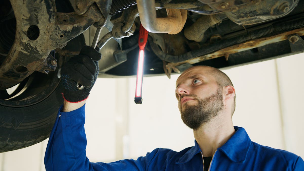 Don't Attempt These 5 Car Maintenance Tasks Unless You Are A Professional 3 Mechanic focusing on vehicle maintenance under a car lift in a garage.