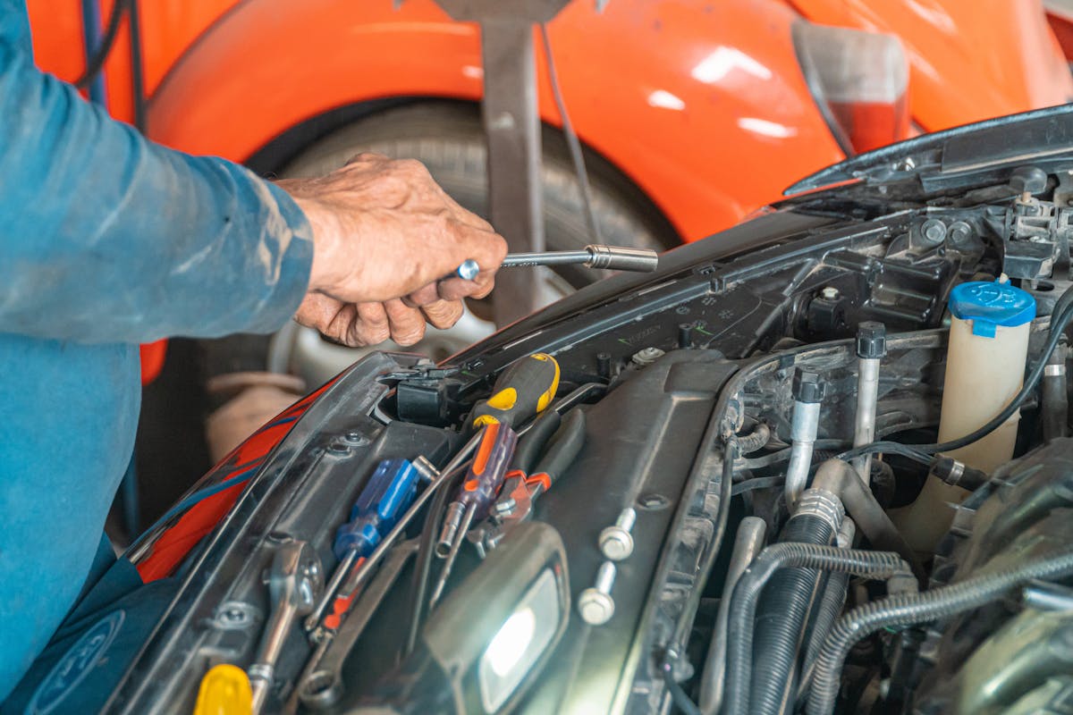 Don't Attempt These 5 Car Maintenance Tasks Unless You Are A Professional 1 Mechanic performing maintenance on a car engine in a garage setting, using various tools.