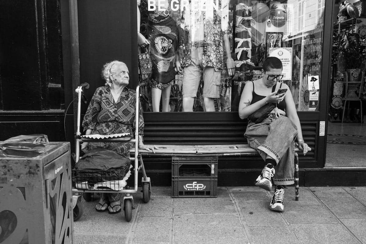 10 Baby Boomer Behaviors That Annoy Millennials and Gen Z 5 Monochrome street photo of two women sitting outside a clothing store, one using a phone.