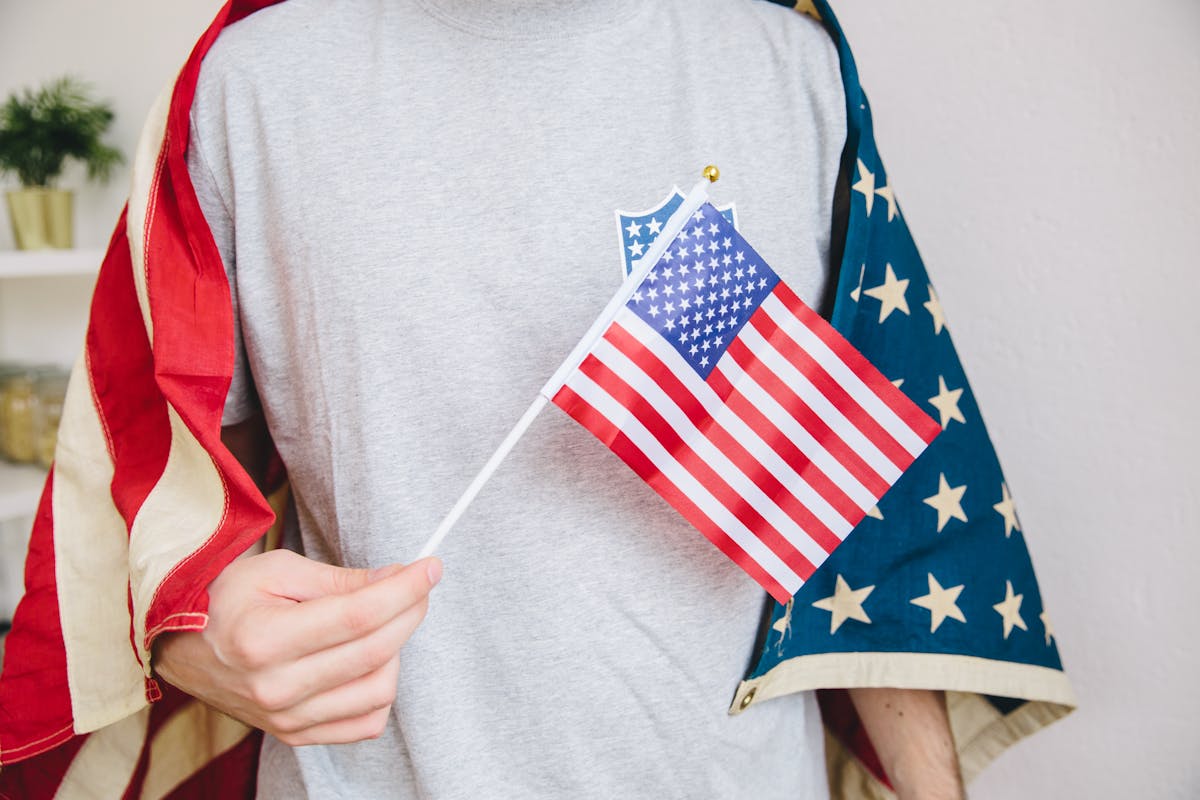10 Shocking Ways Belgians Are Turning Against the U.S. While Softening Toward China 1 Person holding a small American flag, draped in a larger US flag indoors.