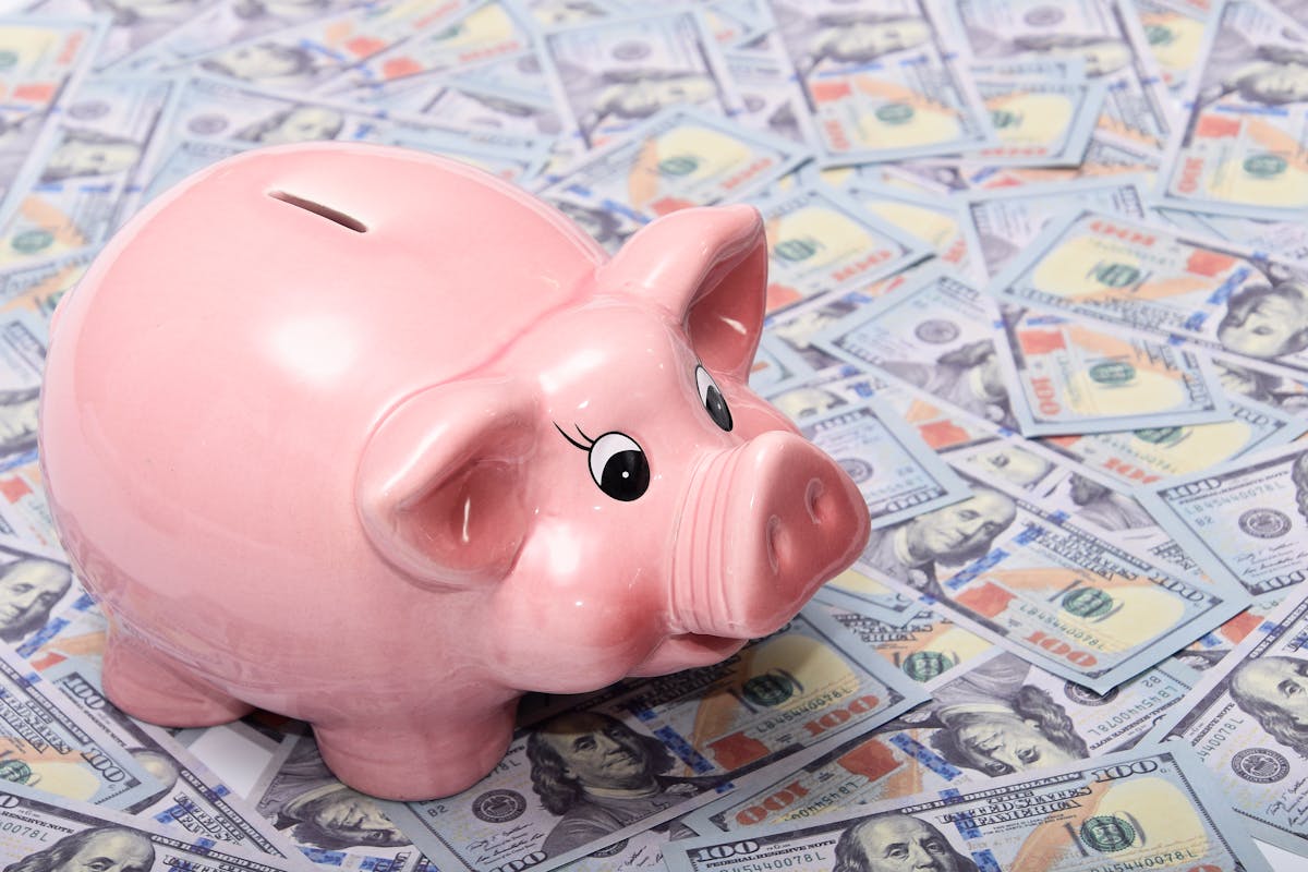 8 Money Mistakes You Need to Avoid to Protect Your Financial Future 1 Pink ceramic piggy bank placed on a spread of US dollar bills symbolizing savings and financial security.