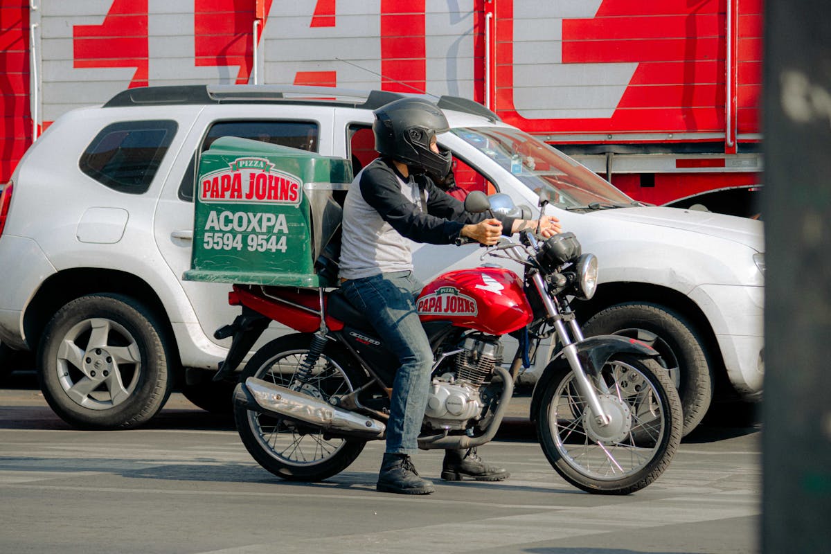 7 Unusual Fast-Food Scandals and Lawsuits That Shook the Industry 4 Pizza delivery rider on a motorcycle waits at a busy city street intersection.