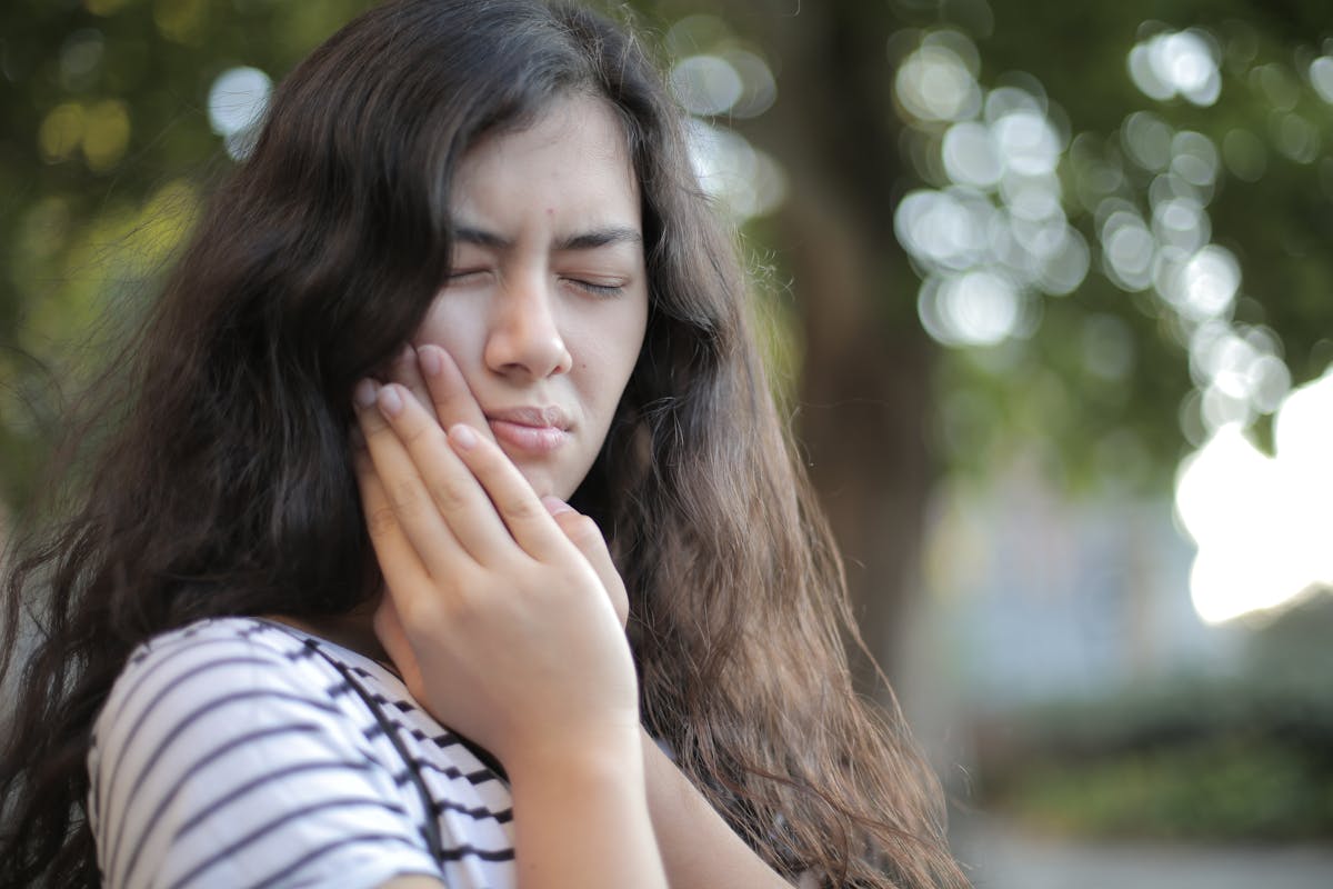 8 Odd Health Symptoms We Should Never Ignore 1 Portrait of a young woman feeling toothache, showing discomfort outdoors with a pained facial expression.