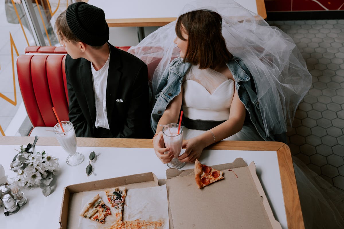 10 Weird Marriage Laws That Are Still Real in 2026 2 Quirky wedding photo of a bride and groom enjoying pizza and milkshakes in a retro diner.
