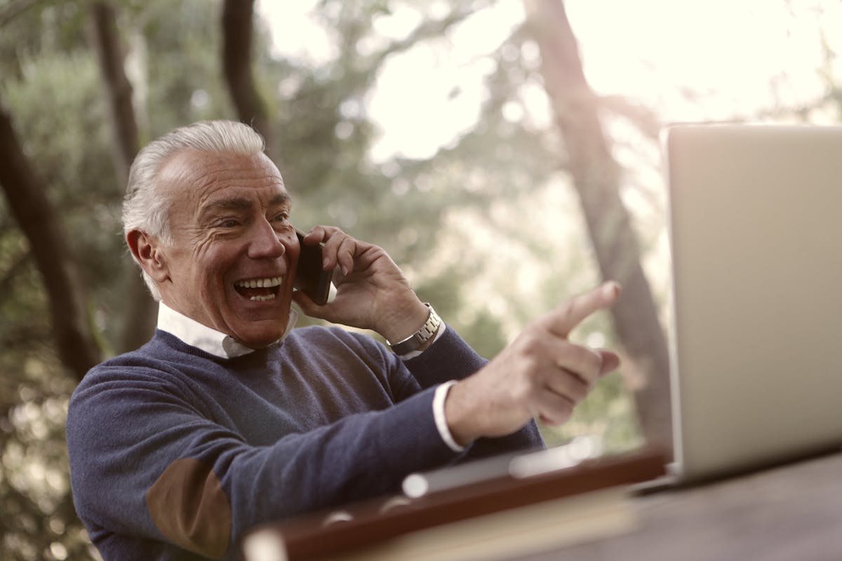 10 Common Scams Targeting Seniors and How to Avoid Them 2 Senior man enjoys phone call and laptop in a sunny outdoor setting.