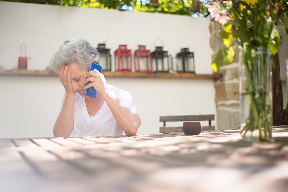 10 Common Scams Targeting Seniors and How to Avoid Them 1 Senior woman expressing grief while on a phone call outdoors in a serene setting.