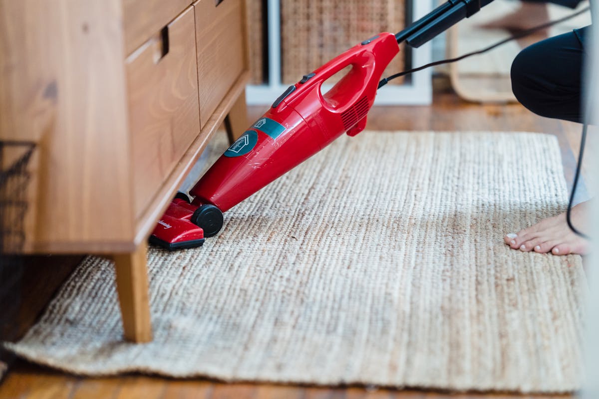 10 Cleaning Mistakes That Make Your Home Dirtier 3 Side view of a person using a red vacuum under furniture on a rug for effective cleaning.