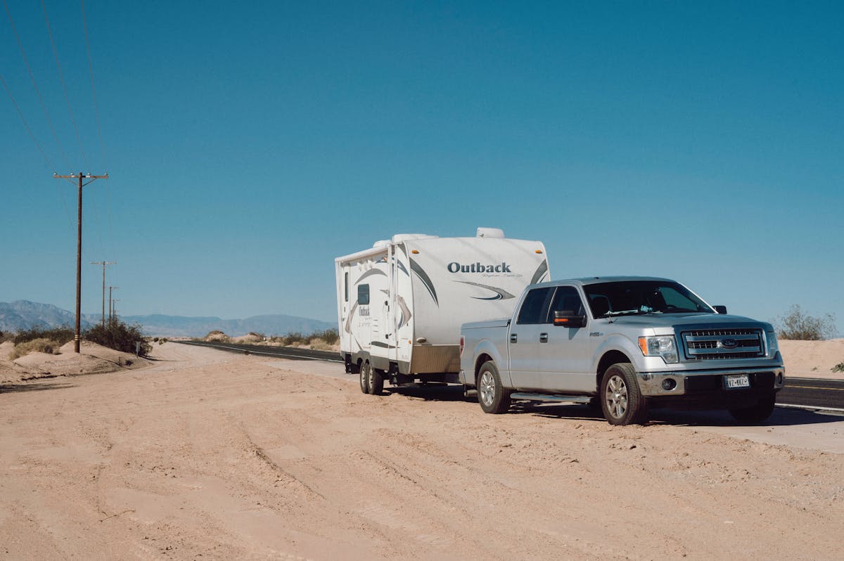 10 People Who Should Not Buy a Truck 1 Silver truck towing an Outback trailer on a desert road under clear blue skies.