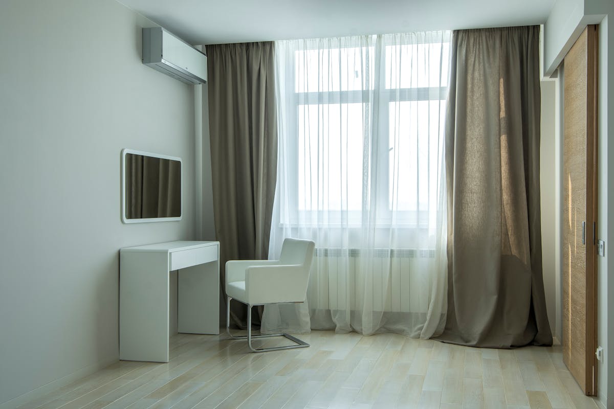 10 Decorating Mistakes Designers Notice Immediately 3 Sleek minimalist room with white desk, chair, and large window with sheer curtains.