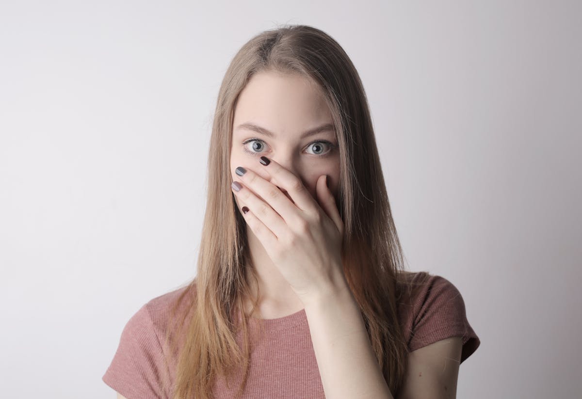 10 Unusual Signs Your Body Is Healthier Than You Think 2 Surprised young woman covering mouth with hand and looking at camera while standing against gray wall background