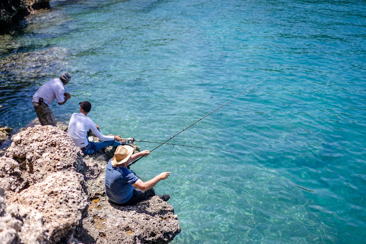 10 Cheap and Fun Bachelor Party Ideas 2 Three men fishing on a rocky shore by a clear ocean on a sunny day.
