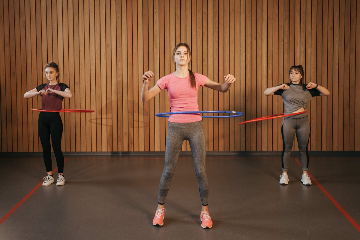 12 Crazy Workouts to Try This Summer That Actually Make Fitness Fun 1 Three women in activewear using hula hoops for fitness indoors.
