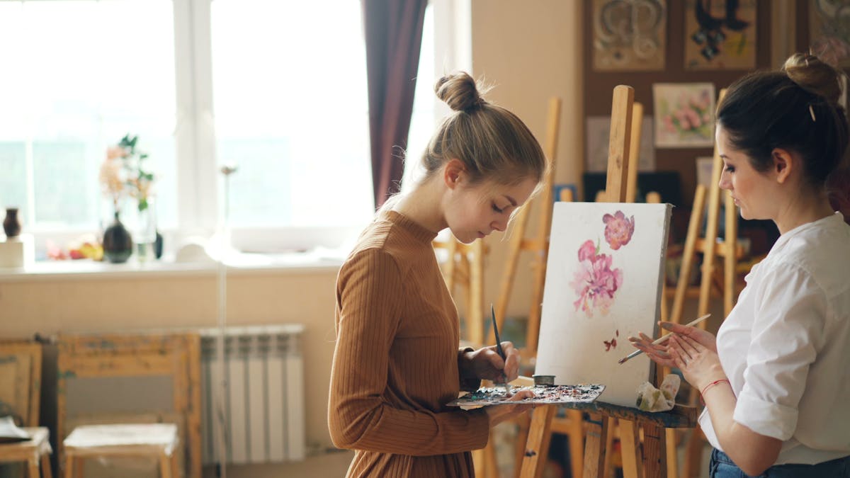 12 Financial Myths to Avoid Teaching Your Adult Children 4 Two young women artists painting floral artwork on canvas in well-lit studio.
