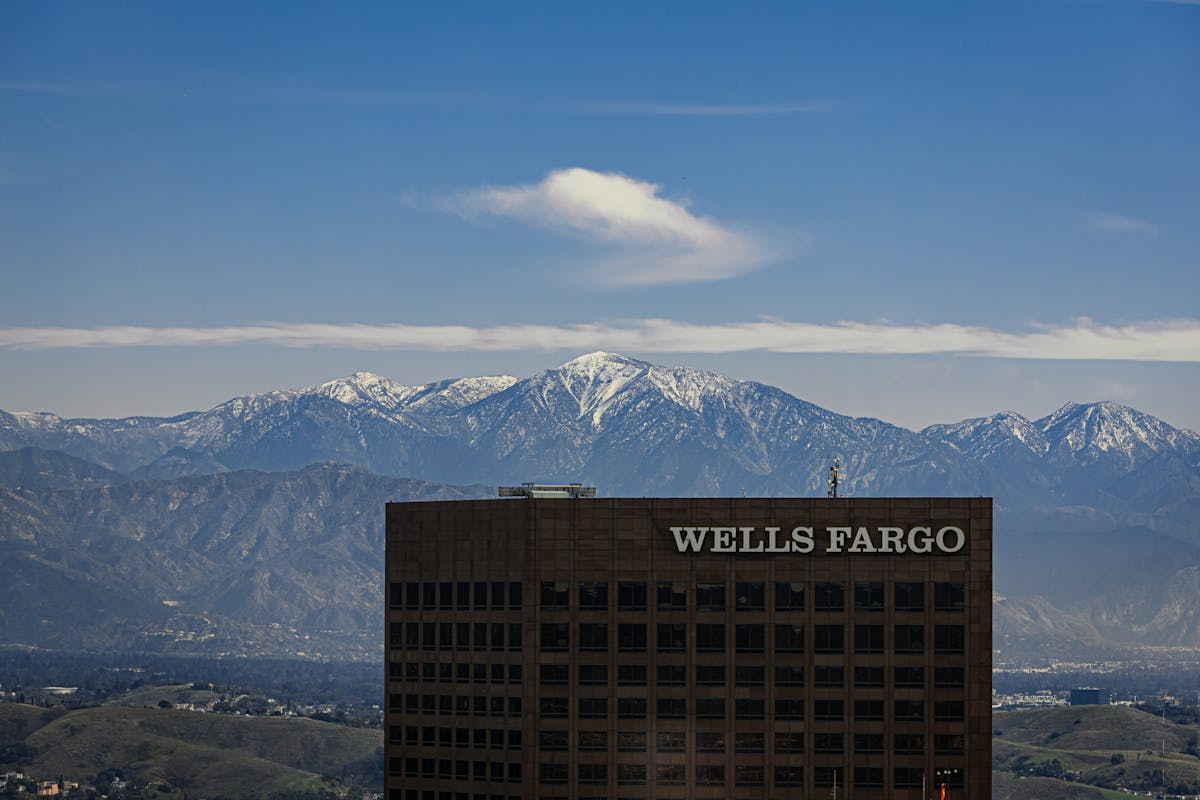 10 Bizarre Schemes Corporations Have Tried To Get Away With 1 View of a Wells Fargo building with snow-capped mountains in the background under a clear blue sky.
