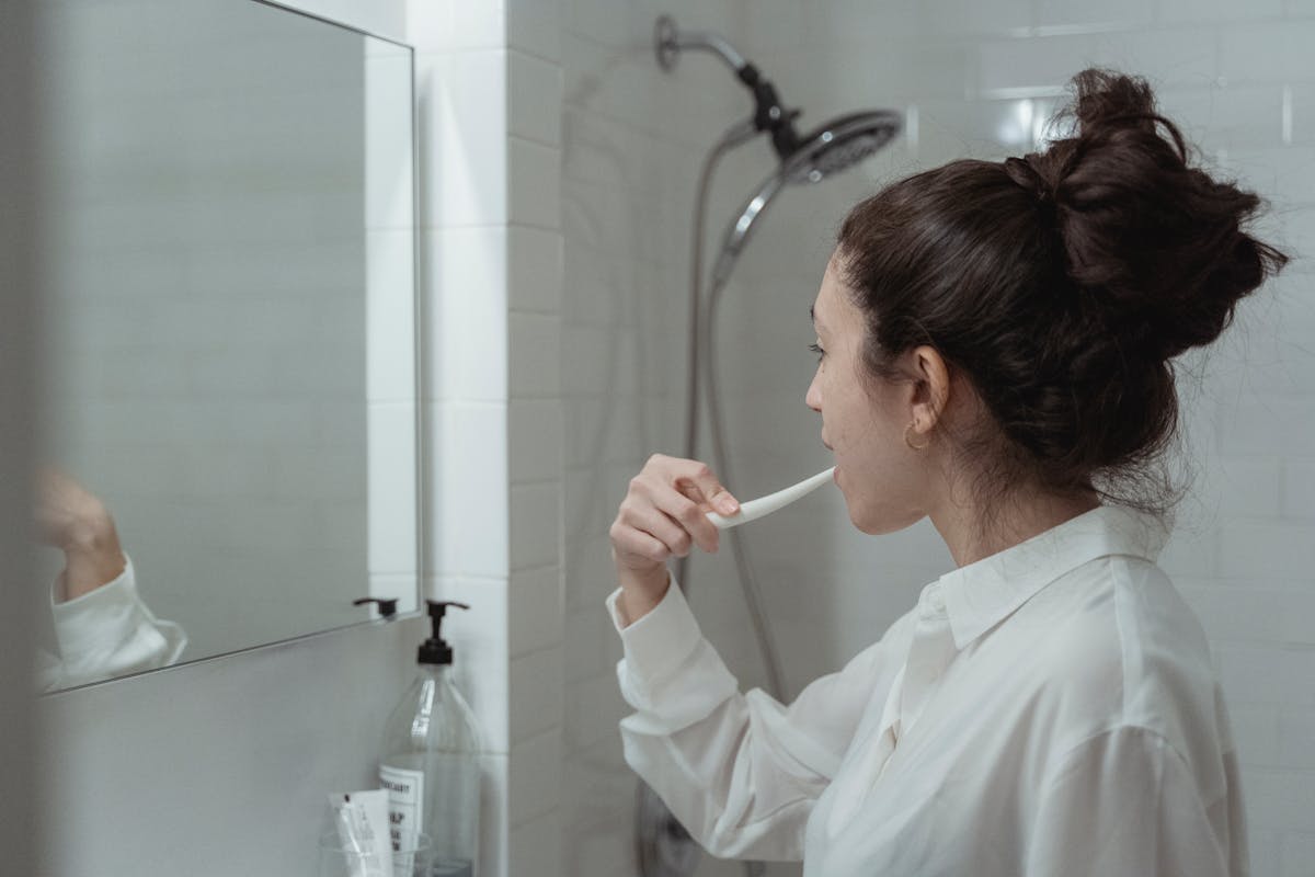 10 Unusual Signs Your Body Is Healthier Than You Think 4 Woman brushing teeth in a modern bathroom, promoting daily oral health habits.
