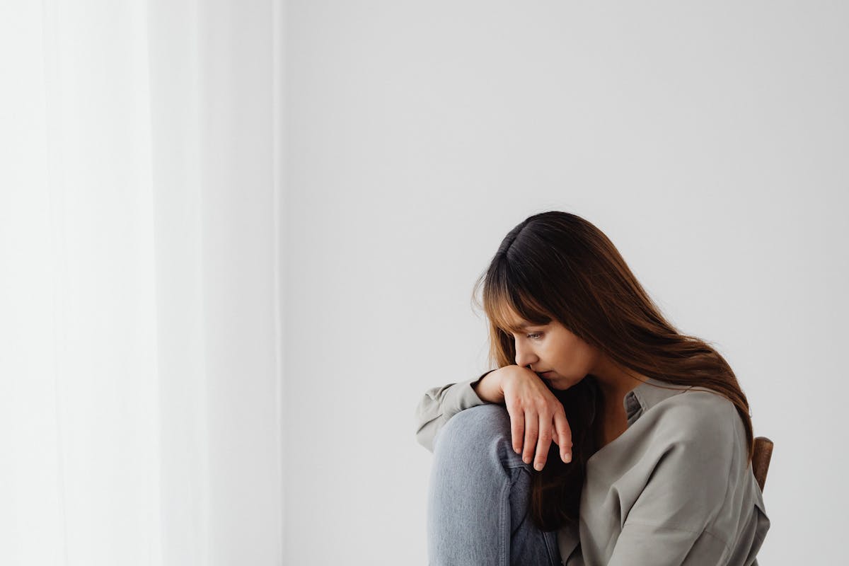9 Dangerous Health Conditions Affecting People Over 60 2 Woman sitting indoors, looking down with hand on knee, reflecting emotions.