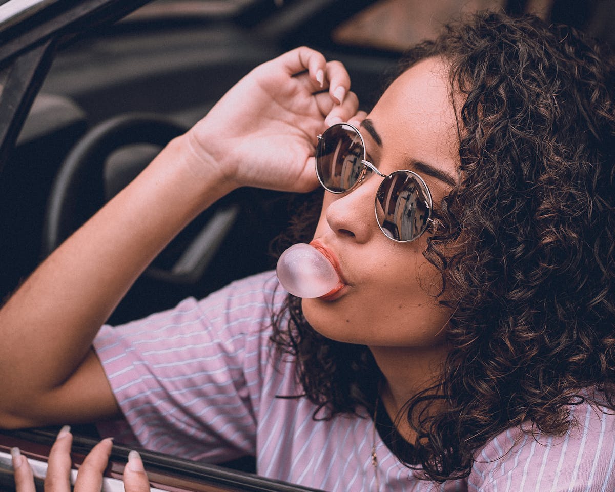 11 Strange Laws From Around the Globe That Will Make You Raise an Eyebrow 2 Woman with curly hair and sunglasses blowing gum in car, exuding style and confidence.