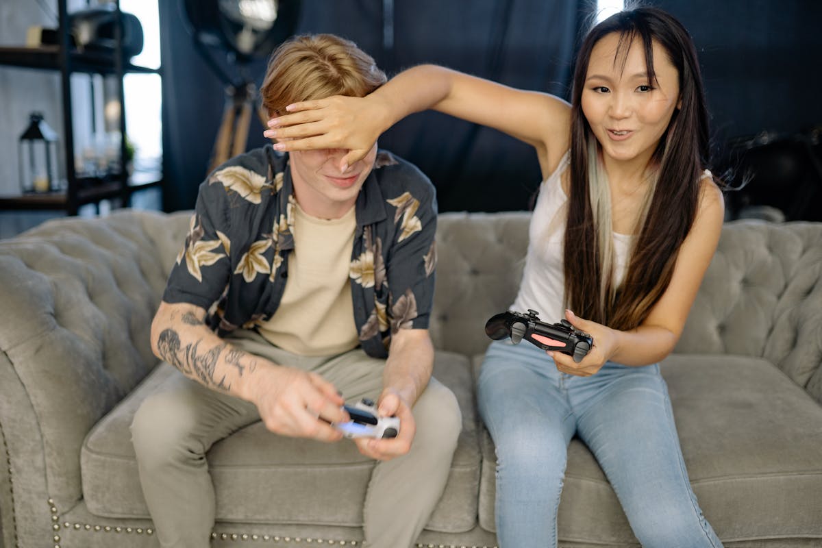 10 Mistakes to Avoid for a Stronger, Healthier Relationship 2 Young friends playfully gaming together on a sofa, enjoying leisure time indoors.