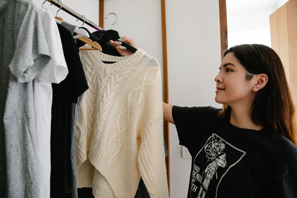9 Mistakes to Avoid When Preparing for Summer 1 Young woman selecting a knitted sweater from wardrobe indoors.