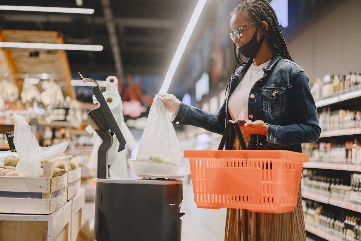 10 Jobs Robots Are Taking From Humans 1 Young woman wearing a mask shops in a modern grocery store with a basket and fresh produce.