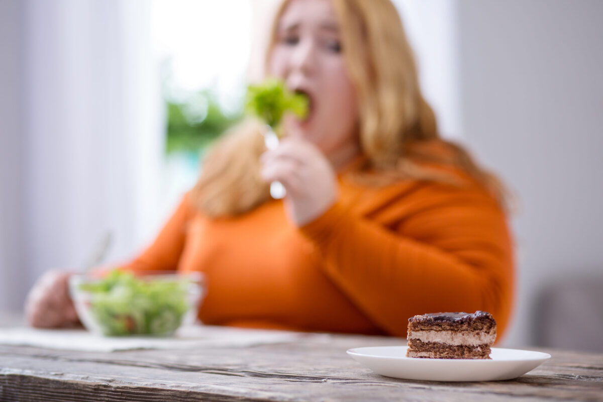 My diet. Miserable stout woman looking at dessert and having healthy breakfast