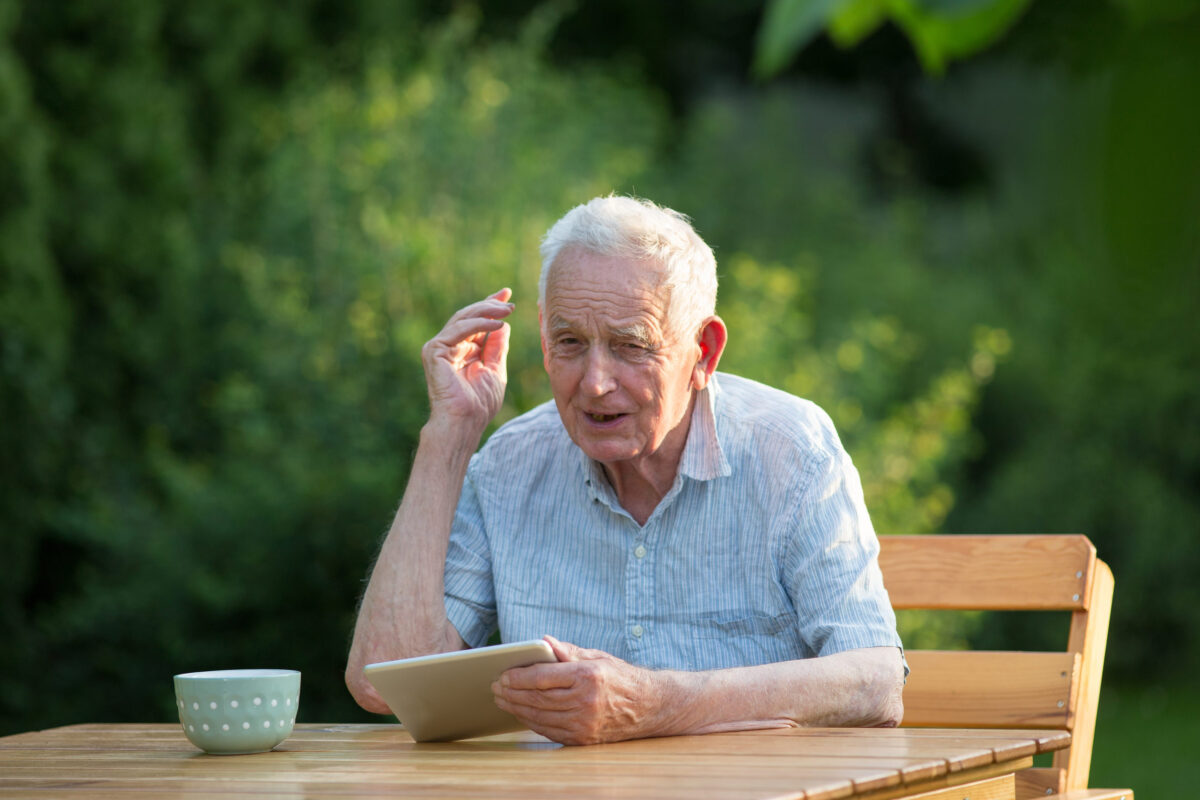 Senior man sitting at table in garden,looking at tablet and feeling unhappy