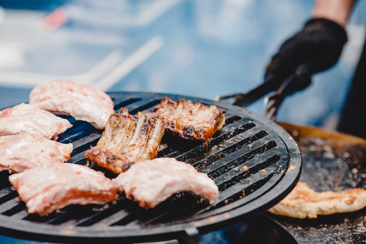 Pork ribs and steak cooked on grill, open fire street food festival.