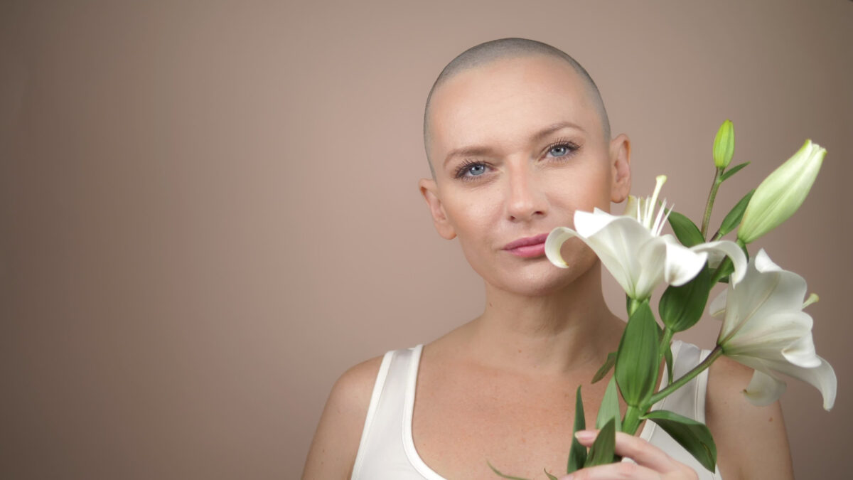 beautiful smiling bald girl sniffs a white lily. beige background, copy space