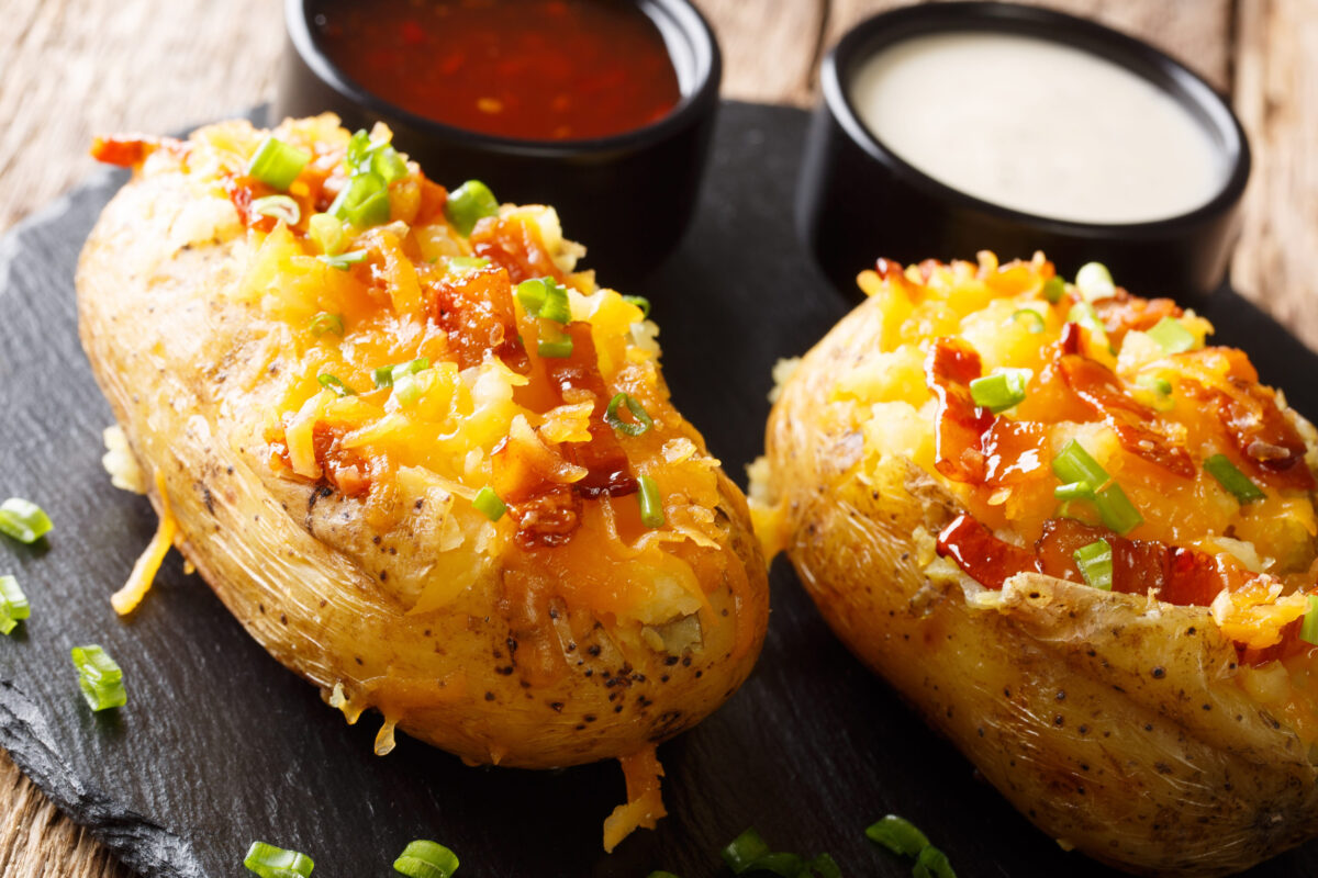 Tasty hot stuffed potatoes with cheddar cheese, green onions and bacon close-up on the table.
