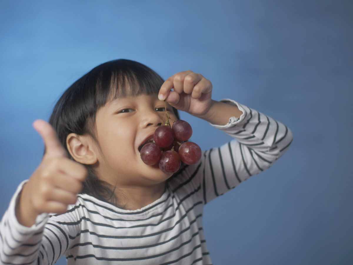 Portrait of little Asian girl enjoying grapes, young girl eat fruit