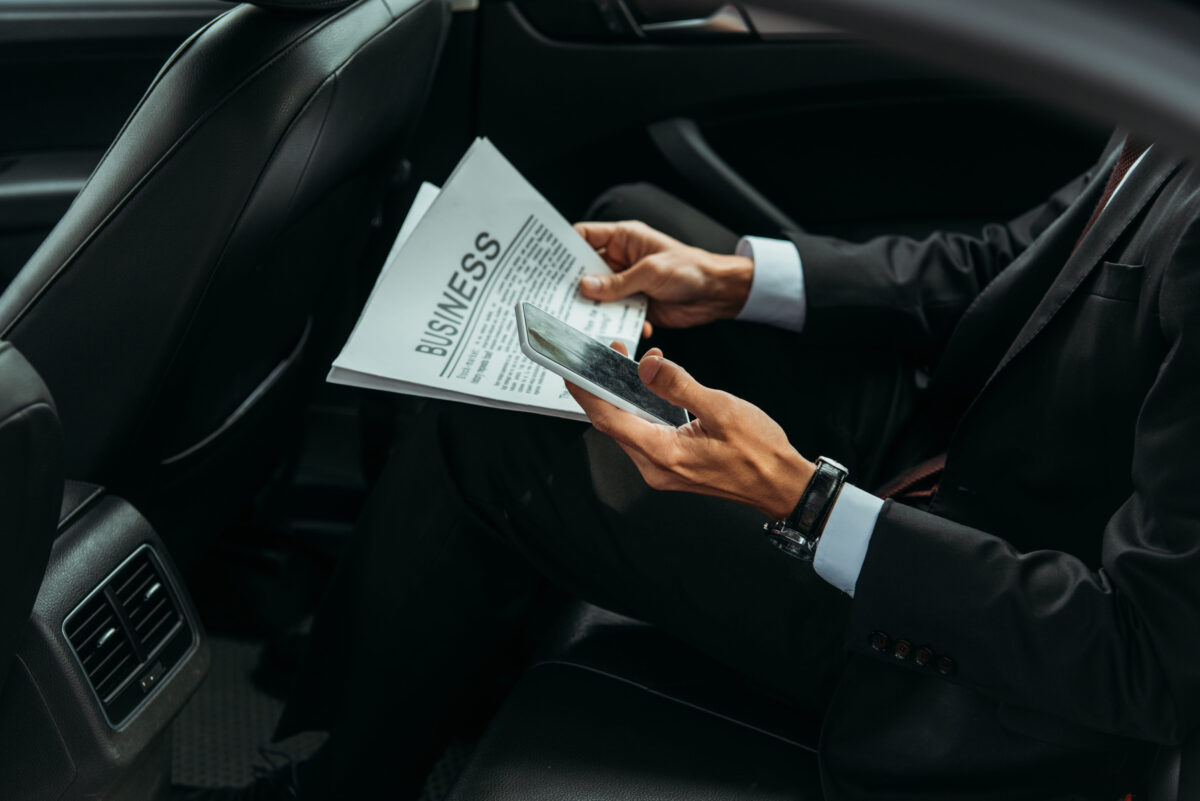 Cropped view of businessman holding newspaper and smartphone in taxi