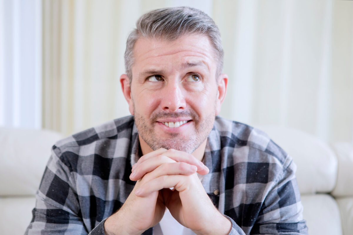 Handsome middle age caucasian man propping his chin with both hands while smiling at home