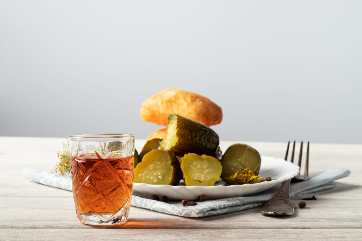 on a wooden table is a glass of cognac, a snack of a piece of dark chocolate and a bottle of alcohol
