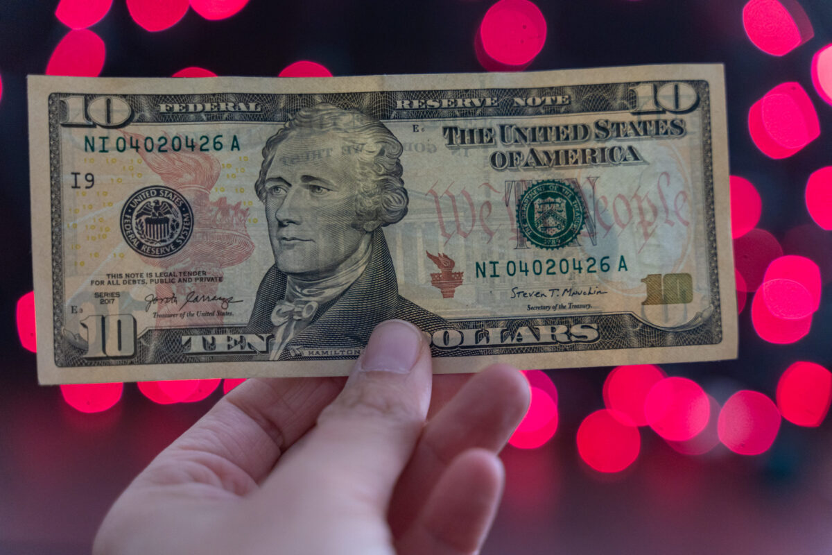 8 Sad Reasons Why Most Americans Want to Leave the Country 1 Hand holds up a ten dollar bill - United States Currency. Red bokeh in background with copyspace