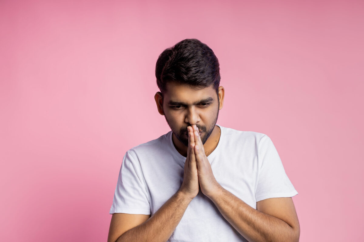 8 “Gentleman” Habits That Can Make Men Look Insecure and Highly Desperate 1 Young religious indian unshaven man wearing white t shirt, keeping palms together, looking down, praying, hoping for best, isolated over in pink background. Belief concept.