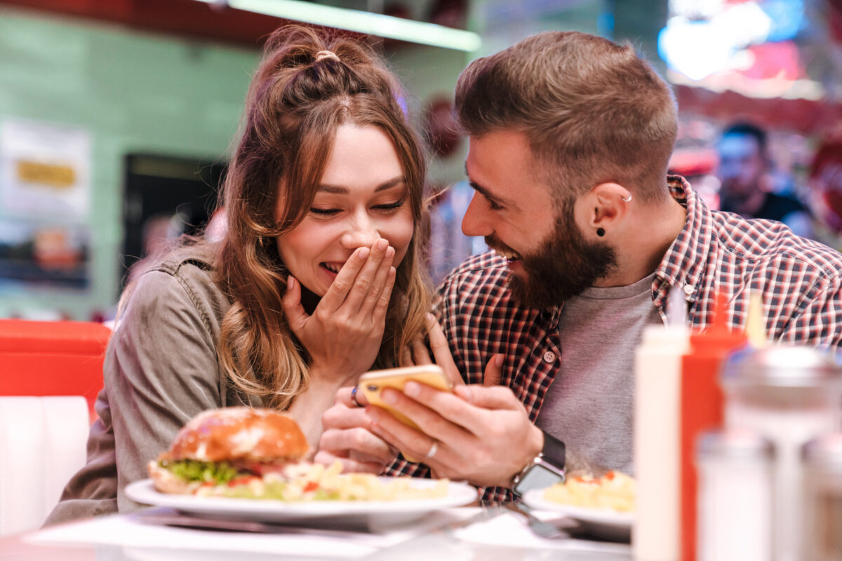 8 Ways Constant Texting is Destroying Your Relationship 2 Photo of a cute happy optimistic young loving couple in retro bright street food cafe using mobile phone.