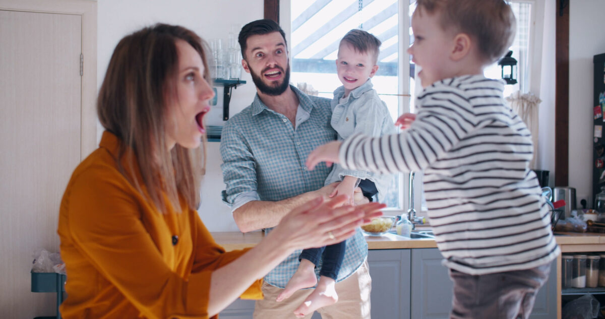 Happy young Caucasian mother and father playing with two little sons in the kitchen, family fun time at home slow motion