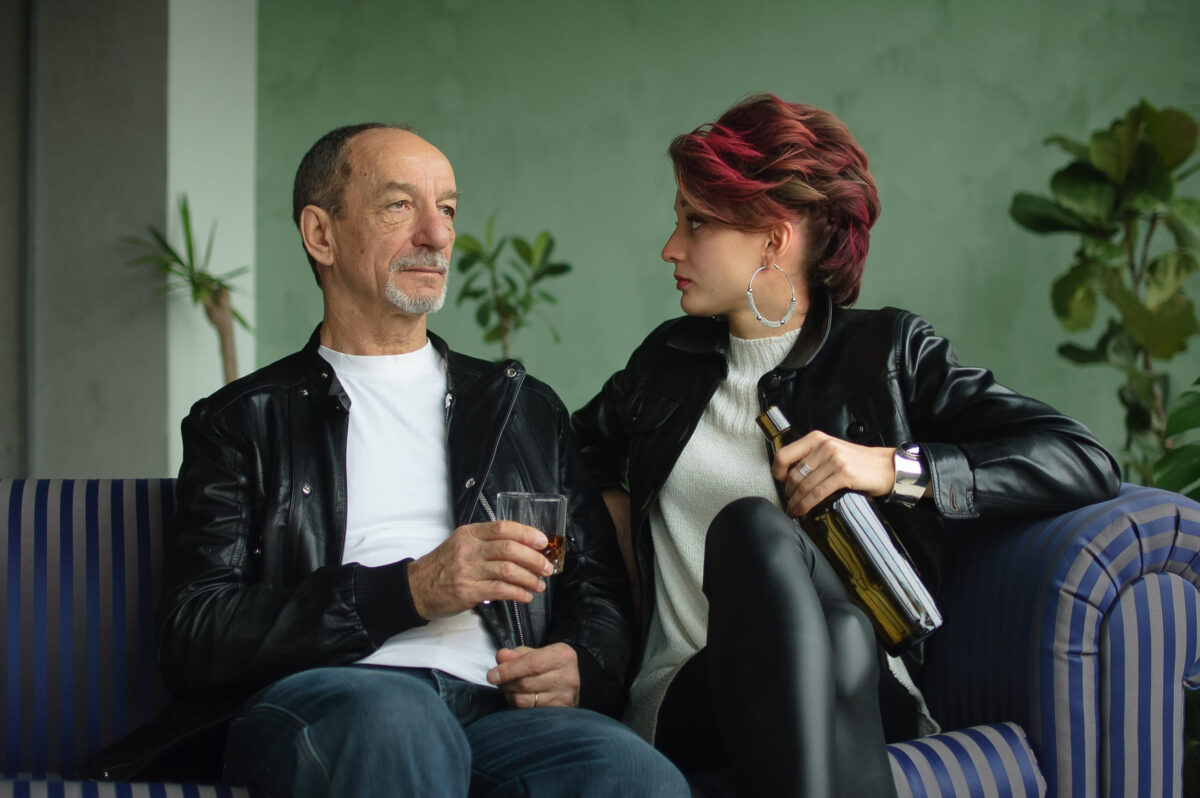 10 Reasons Why Many Men Prefer Dating Younger Women compared to older ones 3 Senior father is drinking with his adult daughter sitting on blue sofa in loft style room, man holds glass of whisky, woman holding bottle in her hand, alcohol addiction concept