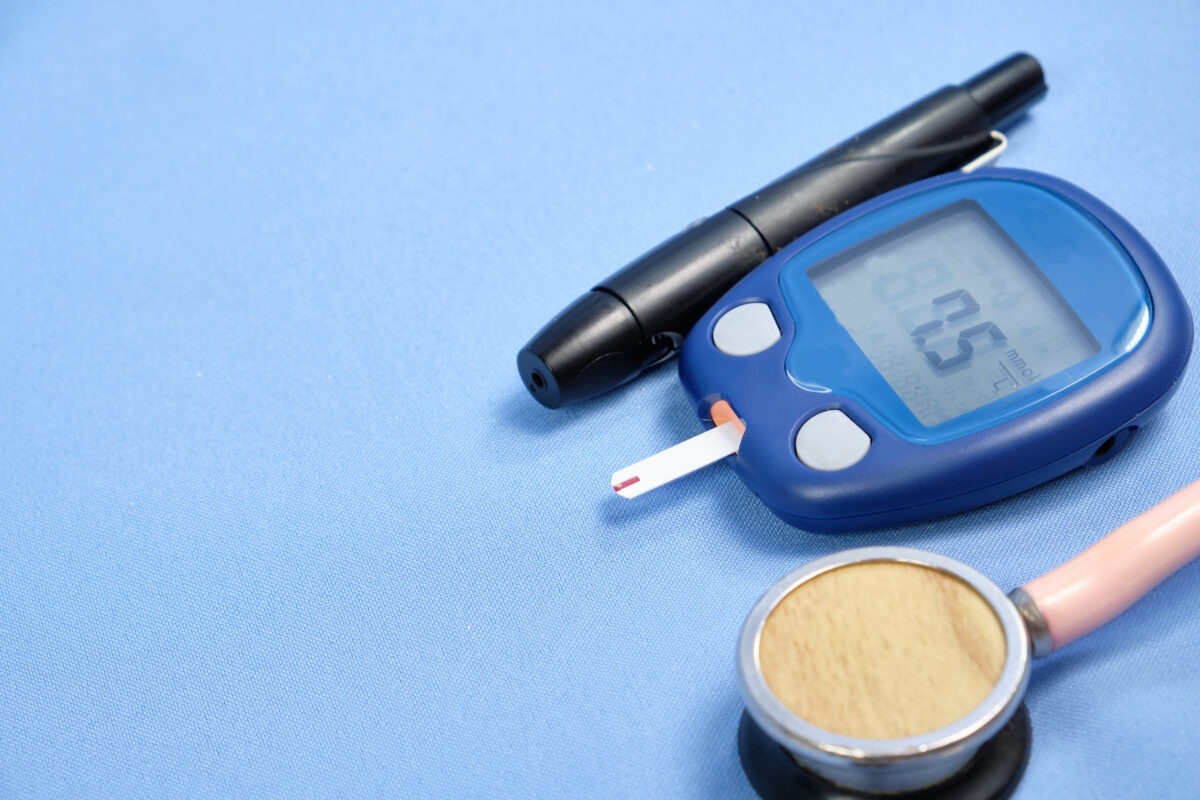 The glucometer with the test strip on a blue background.