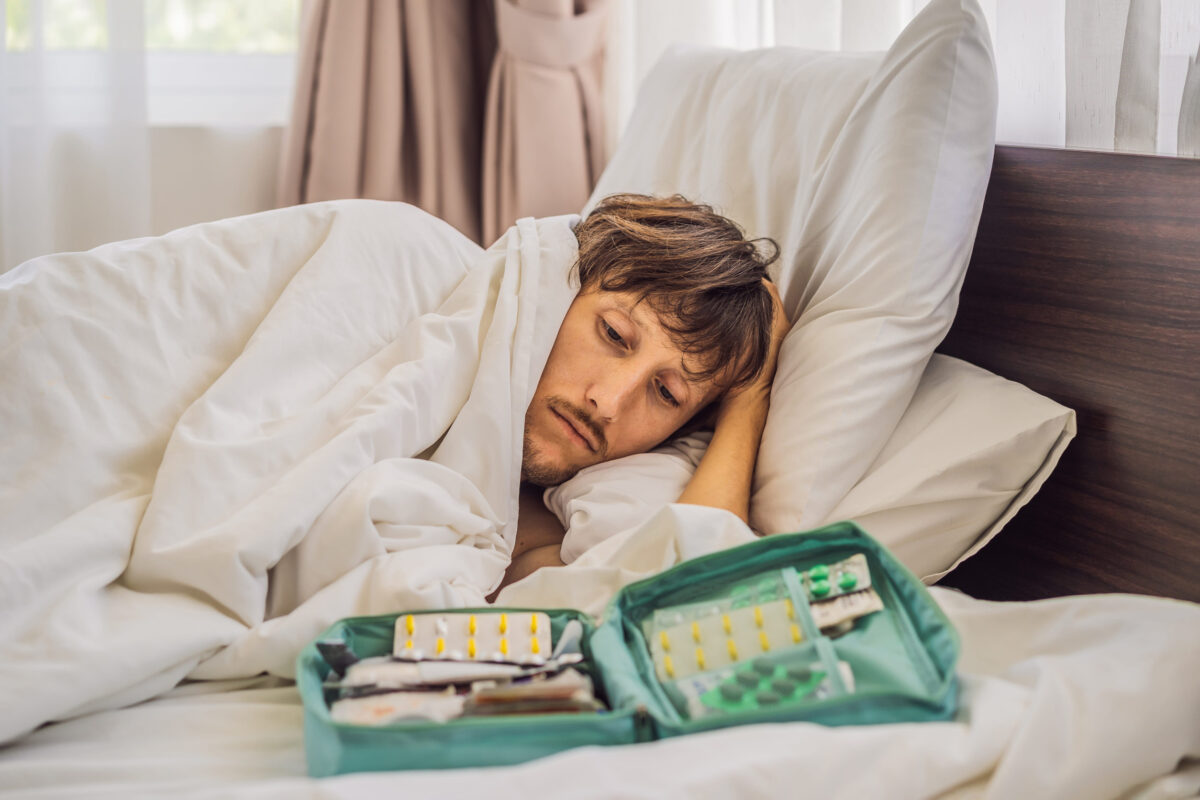 Male patient is sick while lying in his bed and calls an online doctor through a gadget