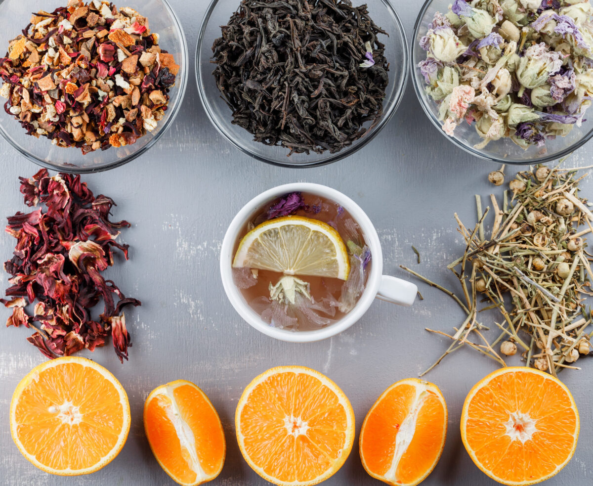 Lemony tea in a cup with oranges, herbs flat lay on a plaster background