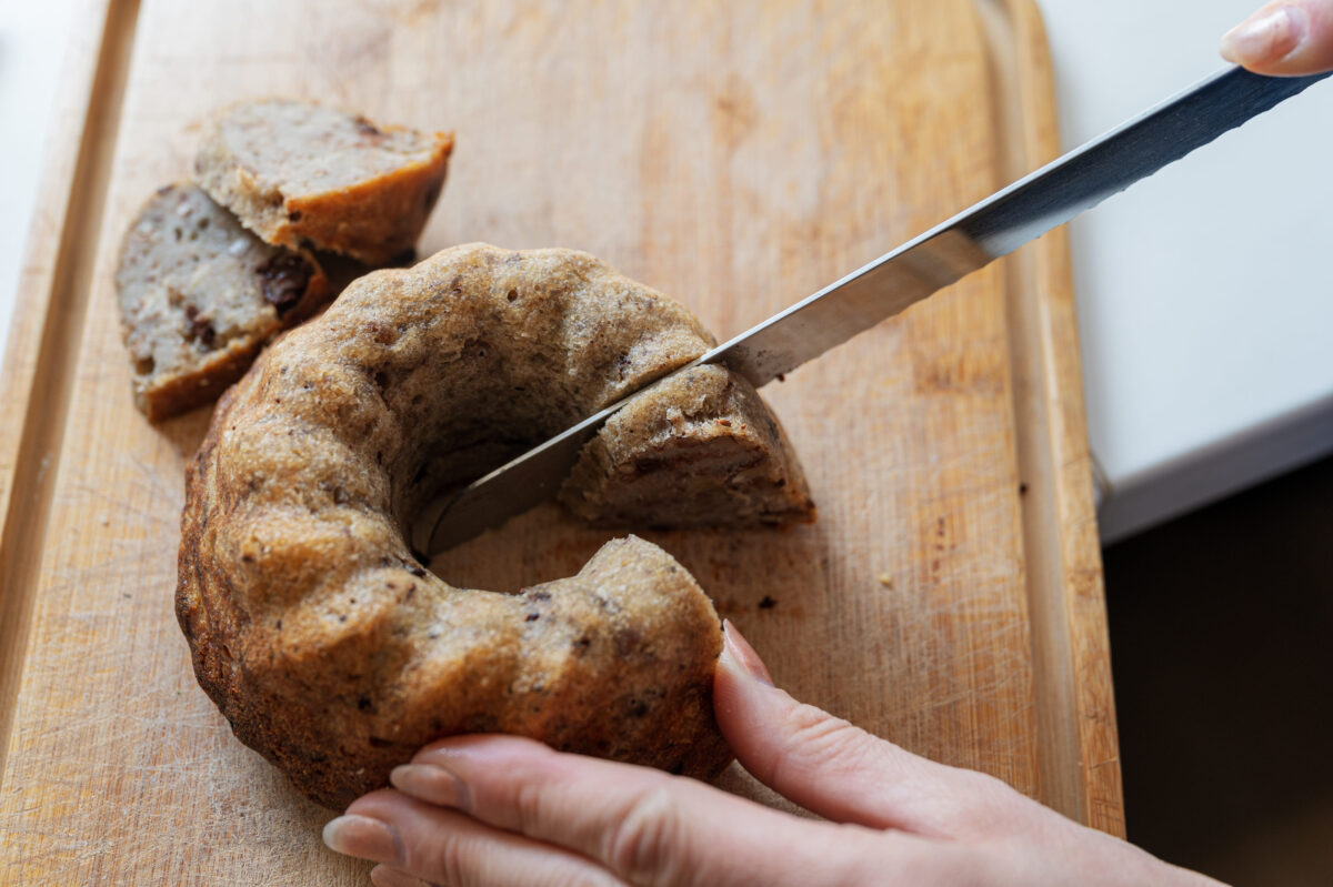 Closeup view of a woman cutting freshly baked home made vegan bread on a wooden board.