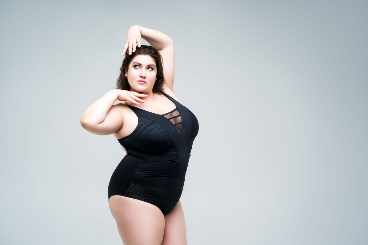 9 Backhanded Compliments Curvy Women Are Tired of Hearing 1 Sexy plus size fashion model in black one-piece swimsuit, fat woman in lingerie on gray background, body positive concept