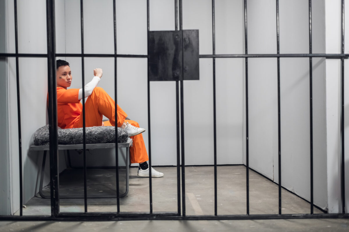 Solitary cell with a criminal in an orange robe in an asian prison. Copy space. Sad emotions of a young guy