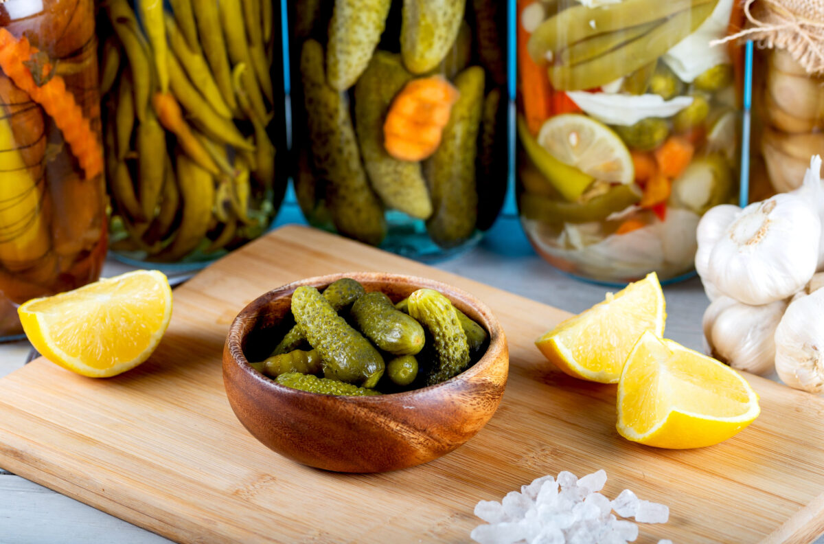 Bowl of pickled cucumbers and jars of pickled vegetables on wooden