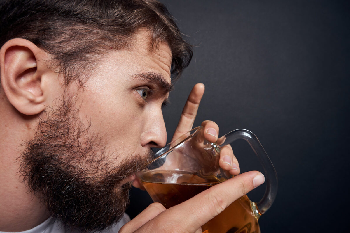 man with a mug of beer in a white t-shirt emotions lifestyle drunk on a dark isolated background