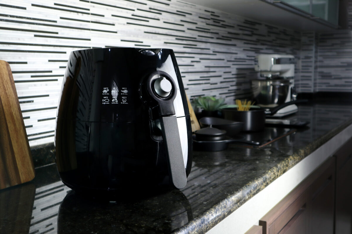 a black deep fryer or oil free fryer , air fryer appliance, is on the black marble table in the nice interior design kitchen of the house