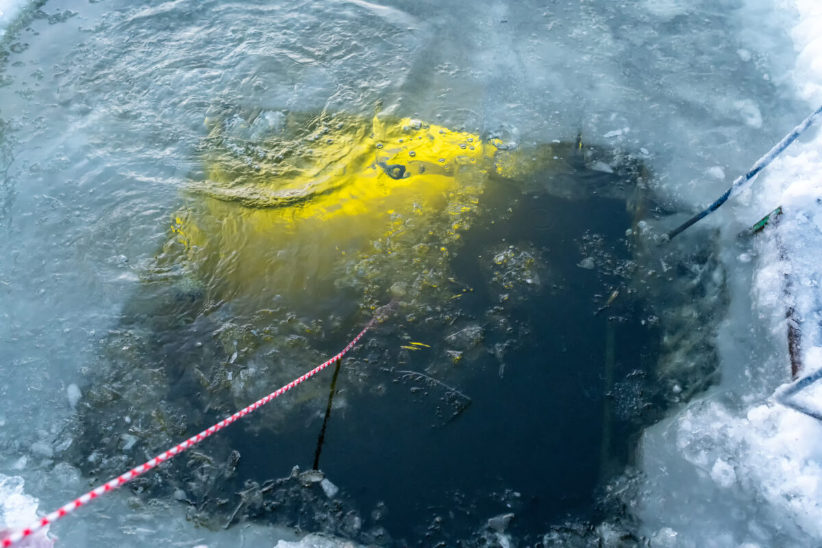 A diver from under the water shines with a flashlight torch an ice hole entry with a for ice scuba diving